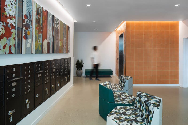 Square LED recessed lights with white trim light an apartment lobby, while cove lights accent pictures above unit mailboxes.