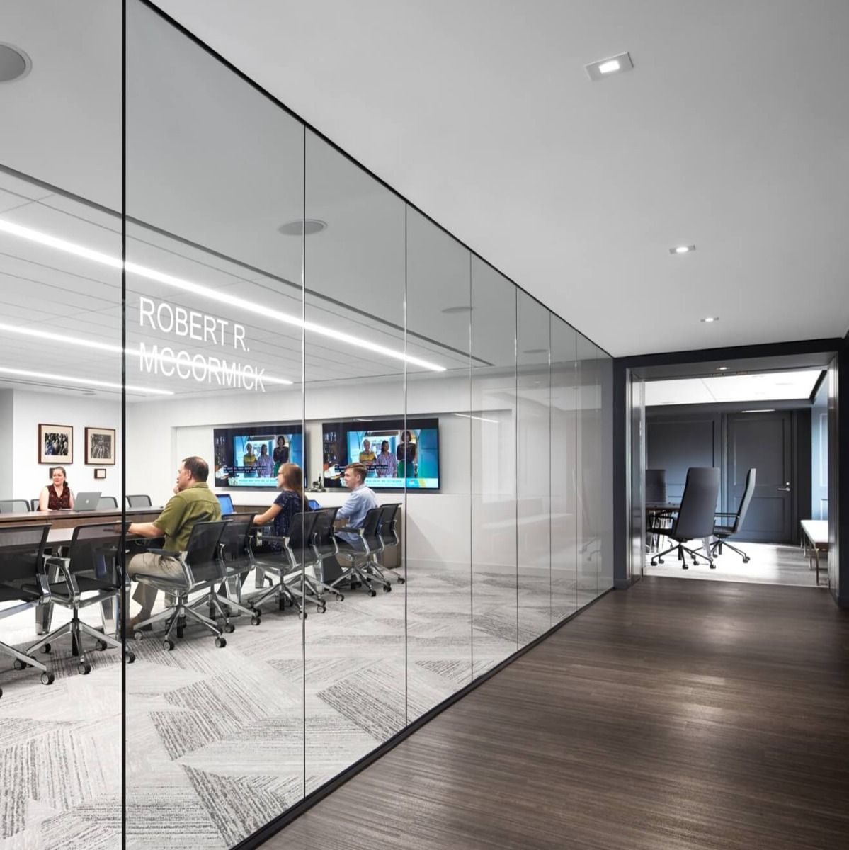 Flanged square LED recessed lights with white trim light a corridor outside an office conference room.