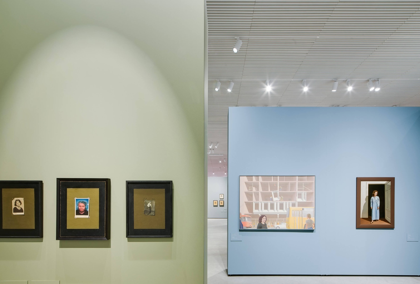 A track channel mounted in a wooden slat ceiling holds white LED track lights to illuminate wall art in a gallery.